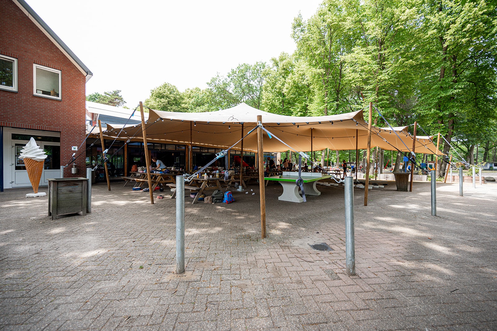Zandkleurige stretchtent als overkapping van een terras bij een recreatielocatie